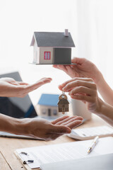 A real estate agent is handing over a small house plan with house keys to the buyer after the...
