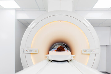 Young patient on automatic table moving outside of closed-type mri machine using noise isolation headphones. Modern equipment, coil on the patient's knee - obrazy, fototapety, plakaty