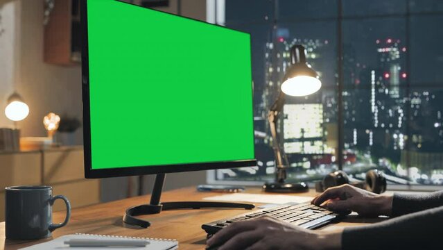 hand moving mouse typing on the keyboard,computer monitor with green screen on desk in the modern home office with window city view