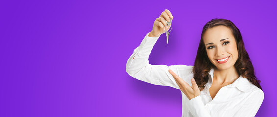 Happy smiling young businesswoman or real estate agent showing keys from new house. Portrait of brunette business woman, isolated on violet purple background.