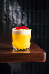 delicious light yellow sour foam cocktail in the etched glass with ice, dark wooden background, vertical, side view