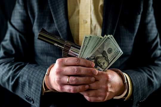 cropped photo of man in suit handing black gun and wad of dollars isolated on black background