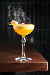 Yellow alcoholic cocktail with white foam. Cocktail glass. Wooden table on background