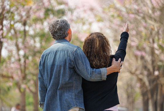 rear view romantic senior couple walking,talking in nature and seeing the flowers on springtime, concept for elderly lifestyle,travel,relaxing,well being,elderly health benefits in nature