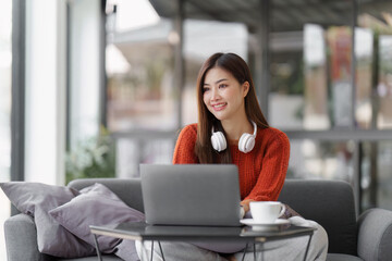 Beautiful Asian Woman smile and relaxing at home and using laptop computer sitting on cozy sofa