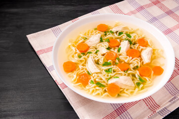 Homemade chicken soup with noodles and vegetables in a white bowl, on a black background.