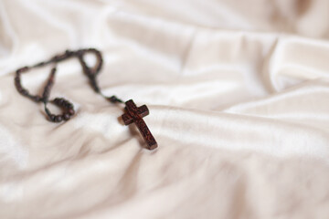 A wooden rosary with crucifix isolated on a beige colored fabric background to represent and symbolize lent, solemn Christian religious observance 
