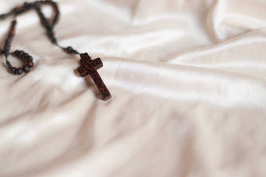 A wooden rosary with crucifix isolated on a beige colored fabric background to represent and symbolize lent, solemn Christian religious observance 