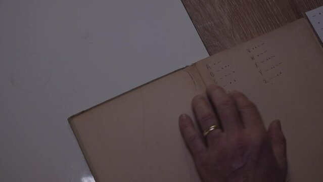 Man following reading morse code dictionary old book hand with golden ring at night close up 4K