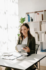 Confident Asian woman with a smile standing holding notepad and tablet at the modern office..