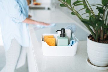 Box with things for cleaning kitchen on background of young woman at home