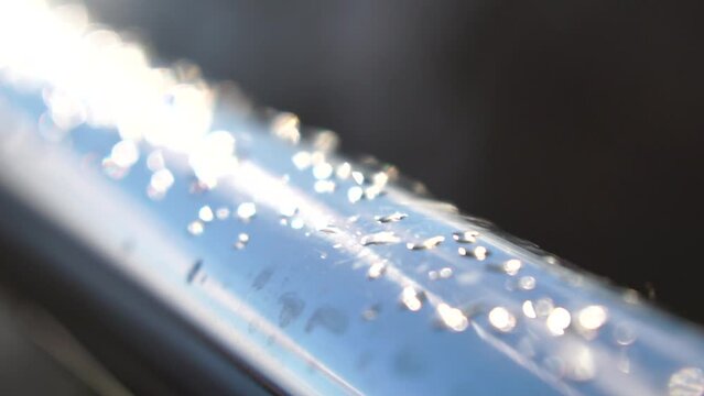 Raindrops on a stainless steel handrail in the park against a blurred bokeh light. Close-up shot. Water droplets from rain dew collecting on a shiny steel chrome pole hand rail railing.