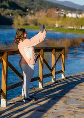 beautiful woman taking photo through a phone on foot of a river copy space for promotional content