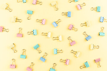 Colorful binder clips on a yellow background. Copy space. Top view.