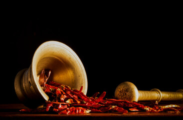 Dried red chilies peppers with metal pestle and mortar against black background