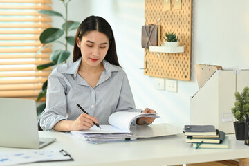 Beautiful young woman accountant examining financial reports at modern workplace
