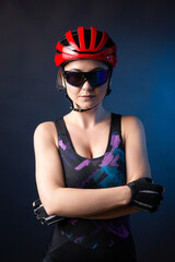 Obraz na płótnie Canvas A young female cyclist wearing a safety helmet and glasses, dressed in a bib shorts poses against a black background in the studio.