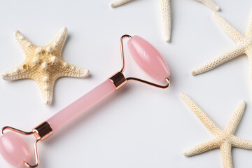 Pink Gua Sha massage tool on a white background, close-up. Rose Quartz jade roller. Facial composition with starfish.