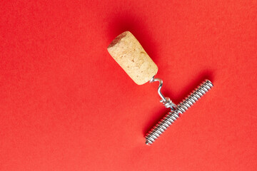 Metal corkscrew screwed into a wine cork on a red background. View from above.