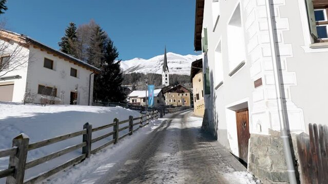 View of a traditional Swiss village streets and houses with mountains in background during a sunny winter day in Zuoz, Switzerland.