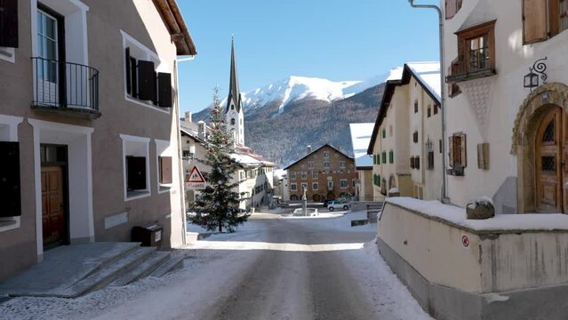 View of a traditional Swiss village streets and houses with mountains in background during a sunny winter day in Zuoz, Switzerland.