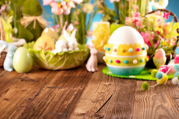 Obraz na płótnie Canvas Easter theme. Easter decorations. Easter eggs in basket and easter bunny. Bouquet of spring flowers. Rustic brown table and blue background.