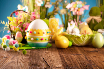 Fototapeta na wymiar Easter theme. Easter decorations. Easter eggs in basket and easter bunny. Bouquet of spring flowers. Rustic brown table and blue background.
