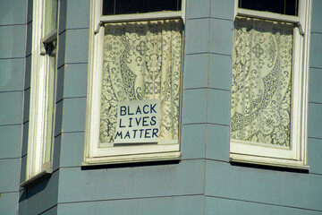 Wooden blue building with white accent window frames with sign in glass window that say black lives...