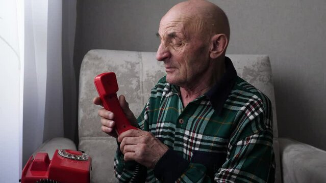 caucasian grandfather sitting on an armchair dials 911 on a vintage wired telephone holding his heart with his hands. a pensioner calls doctor on the phone.
