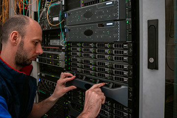 A technician works with computer equipment in a data center. Engineer maintains data storage...