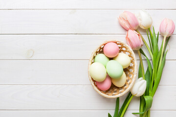 Happy Easter composition. Easter eggs in basket on colored table with yellow Tulips. Natural dyed colorful eggs background top view with copy space