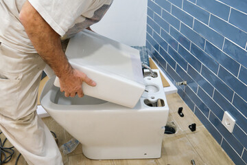 Unrecognizable senior plumber installer installing toilet cistern in a bathroom.