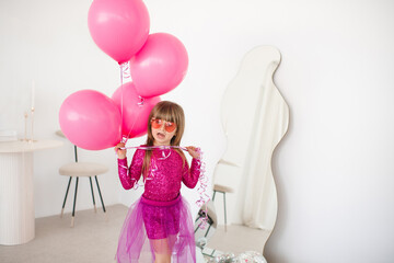 Obraz na płótnie Canvas Cute happy child girl 4-5 year old wear princess dress posing with balloons having birthday party over white in room. Childhood.