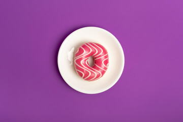 Tasty sweet pink glazed strawberry donut on white round plate from above on violet background. Fast...