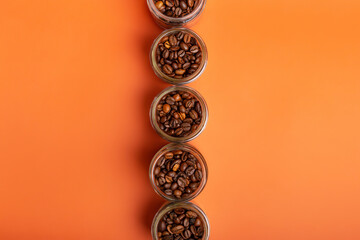 Aromatic roasted arabica and robusta coffee beans in glass small jars on bright orange background. Perfect coffee beans to make tasty coffee beverages such as espresso, americano, cappuccino, latte.