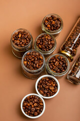 Aromatic roasted coffee beans in small glass jars and in white plates from above in beautiful minimalist composition on brown background. 