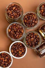 Aromatic roasted coffee beans in small glass jars and in white plates from above in beautiful minimalist composition on brown background. 