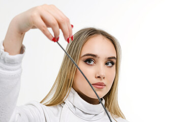 A girl fencer touches the tip of the sword with her palm on a white background.