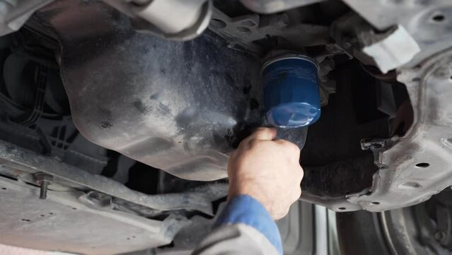 Oil change in the car. A white mechanic unscrews and takes out a car oil filter to replace it with a new one.