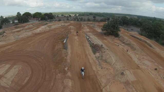 Two motocross riders circulating on a dirt track on a cloudy day while the trator building the ramps. Drone aerial shot.