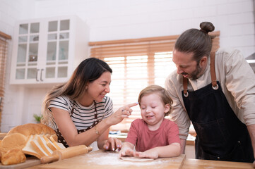 Mom and dad in the kitchen of the house with their small children. Have a good time baking bread and making dinner together.