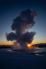 Obraz premium Iceland's great geyser Strokkur in full eruption with mist and smoke backlit and the orange evening or near-dusk sun touching the horizon behind