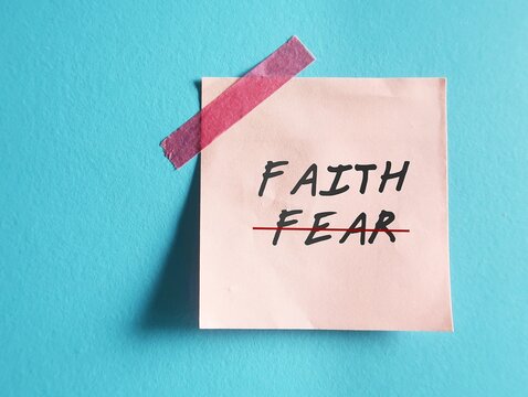Pink note on blue background with text written FEAR , changed to FAITH - concept of positive self talk to overcome inner critic voice and have faith over fear