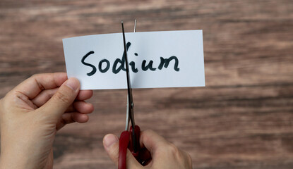 Scissors cutting word sodium on paper - obrazy, fototapety, plakaty