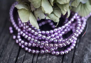 The photo shows hematite beads. This is a natural stone painted in different colors, round and hexagonal. Placed on a wooden board on a background of dried hydrangeas.