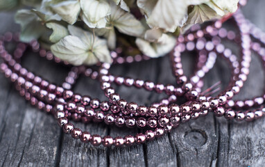 The photo shows hematite beads. This is a natural stone painted in different colors, round and hexagonal. Placed on a wooden board on a background of dried hydrangeas.