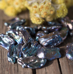 Natural freshwater pearls of various shapes and colors are photographed on a wooden board and a piece of leather.