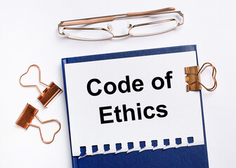 On a white background, golden glasses, paper clips and a notebook with the text CODE OF ETHICS