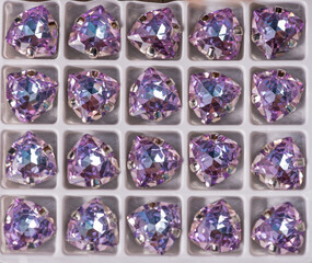 Rhinestones of various sizes and shapes are fixed in goats of gold and silver color, photographed on a wooden board of neutral color.