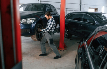 Front left wheel is changing. Man in uniform is working in the auto salon